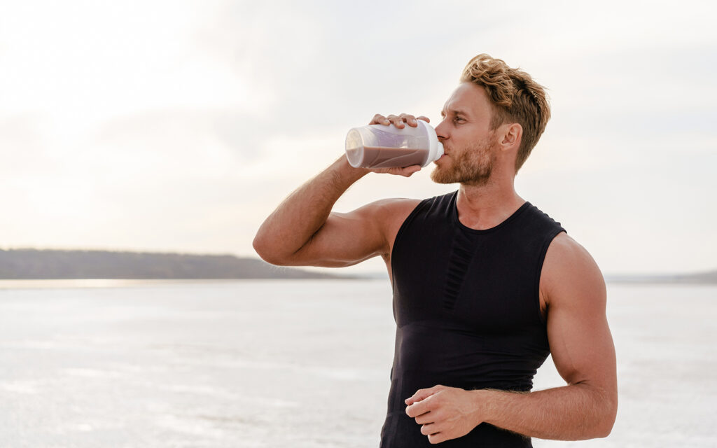 Image of young athletic sportsman drinking protein shake while working out on nature